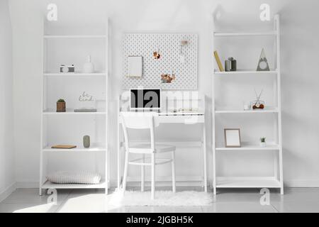 Interior of light office with workplace, pegboard and shelving unit ...