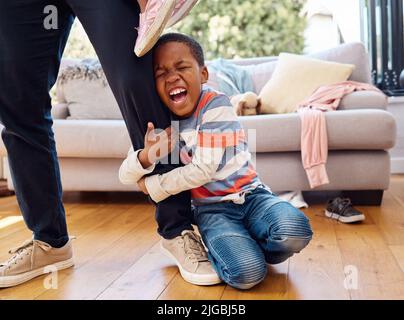 Hes having a bad day. a little boy throwing a tantrum while holding his parents leg at home. Stock Photo