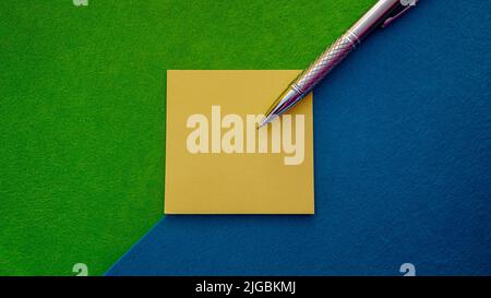 Horizontal composition in which a sticky note block appears with a silver pen on top and all this on a diagonal two-color background Stock Photo