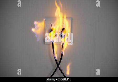 Electrical fire. two plugs in a wall socket catching fire. Stock Photo
