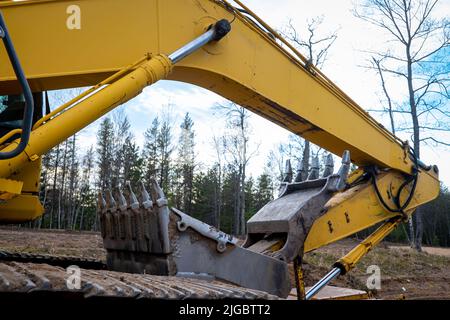 Closeup of a used Boom, Bucket and Hydraulic Cylinder of a yellow Skid Steer Excavator Loader, at a construction job site, in evening light with trees Stock Photo