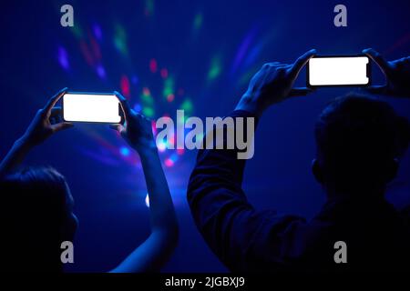 Making memories together. an unrecognisable couple standing together and using their cellphones to film a concert. Stock Photo