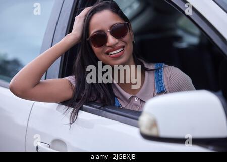 Lets hit the road and have some fun. a young woman leaning out a car window while on a road trip. Stock Photo