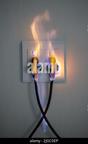 It can happen to anyone. two plugs in a wall socket catching fire. Stock Photo