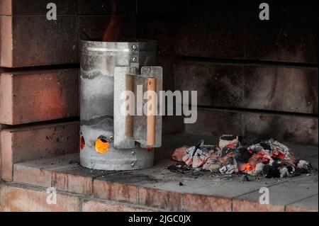 Charcoal Chimney Starter with fire making more embers inside the barbecue, with glowing charcoal embers next to it Stock Photo