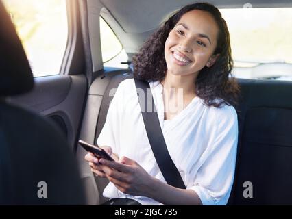 Getting from one place to the next has never been easier. an attractive young businesswoman sending a text while sitting in the backseat of a taxi. Stock Photo