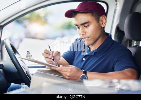Planning his delivery route for the day. a young delivery man writing on a clipboard while sitting in a van. Stock Photo