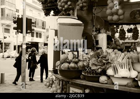 TEL AVIV, ISRAEL - DECEMBER 28, 2017: Urban scene. Fresh detox drink at juice stall. Old ladies cross street; young woman photo on billboard. Sepia Stock Photo