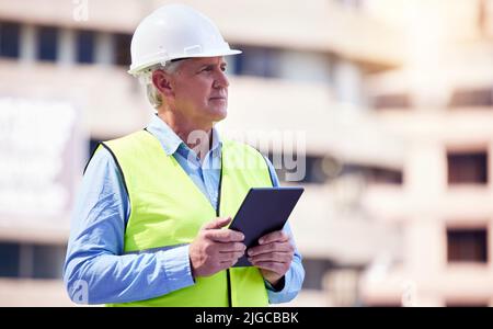 Managing the site online. a handsome mature male construction worker using a tablet while standing outside. Stock Photo