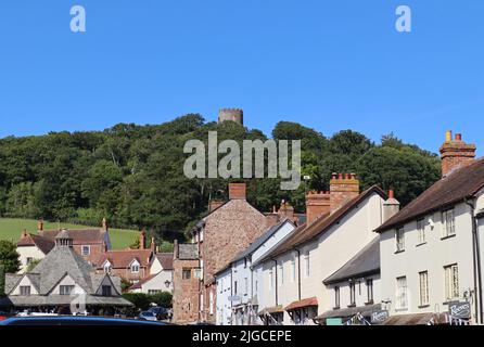 The busy high street of Dunster in Somerset on a beautiful sunny day is overlooked by the magnificent Dunster Castle. This is a National Trust propert Stock Photo