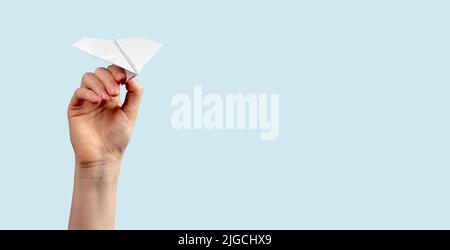 Banner with woman hand throwing origami plane on blue background. Handmade flying paper construction. Freedom, childhood, travelling concept. Copy space. High quality photo Stock Photo