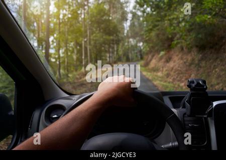 POV. car driver hand on the steering wheel - Road trip in nature in the forest - First person of a person driving on road trip in a natural Stock Photo