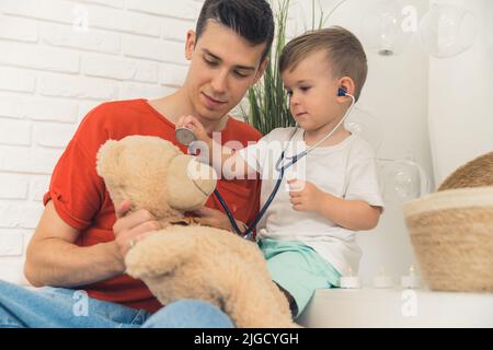 little boy with stethoscope listening to teddy bear breath with his father. High quality photo Stock Photo