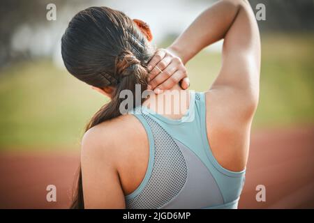 I should have stretched more. Rearview shot of a young athlete experiencing neck pain on a running track. Stock Photo
