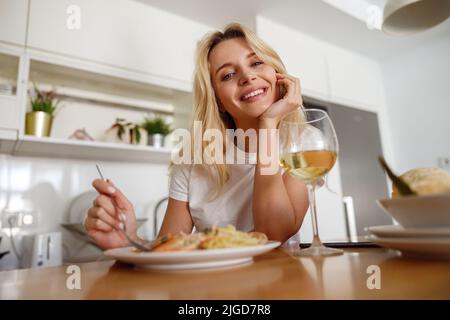 Portrait of cheerful pretty young blonde woman smiling and having pasta with seafood.  Stock Photo