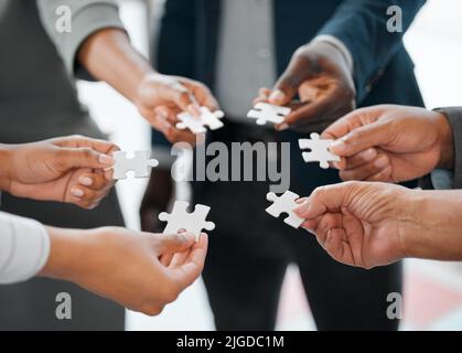 Putting the pieces together. a group of unrecognizable businesspeople holding puzzle pieces while standing in the office. Stock Photo