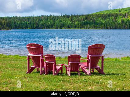 Assortment of four red Adirondack chairs at a lookout point on the shore of Wolfe Lake, in Fundy National Park, New Brunswick, Canada. Stock Photo