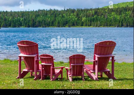 Assortment of four red Adirondack chairs at a lookout point on the shore of Wolfe Lake, in Fundy National Park, New Brunswick, Canada. Stock Photo