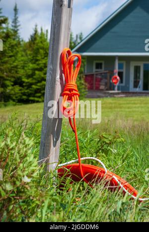 Orange lifebuoy and lifeline rope hanging on wooden pole, on the Wolfe Lake shoreline. Fundy National Park, New Brunswick, Canada Stock Photo