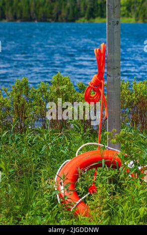 Orange lifebuoy and lifeline rope hanging on wooden pole, on the Wolfe Lake shoreline. Fundy National Park, New Brunswick, Canada Stock Photo