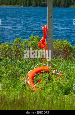 Orange lifebuoy and lifeline rope hanging on wooden pole, on the Wolfe Lake shoreline. Fundy National Park, New Brunswick, Canada Stock Photo