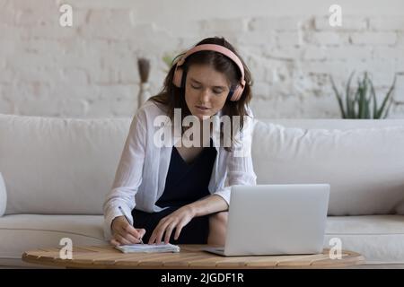 Focused woman in headphones e-learning using laptop at home Stock Photo
