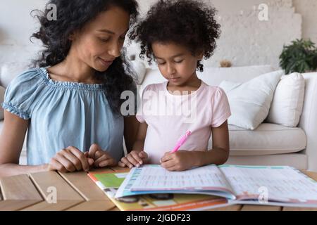 African mom helping to cute daughter with homework at home Stock Photo