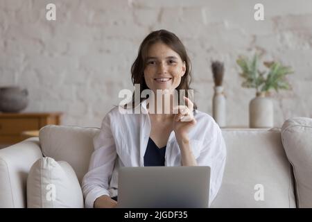 Young woman sit on sofa with laptop looking at camera Stock Photo