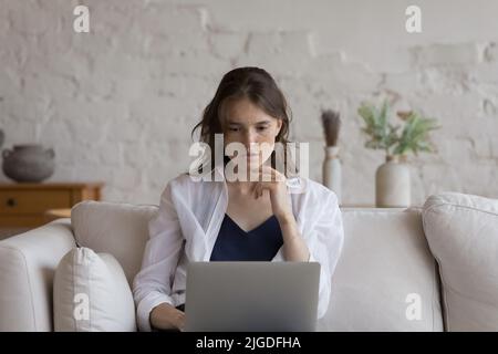Pensive young freckled woman studying or working using laptop Stock Photo