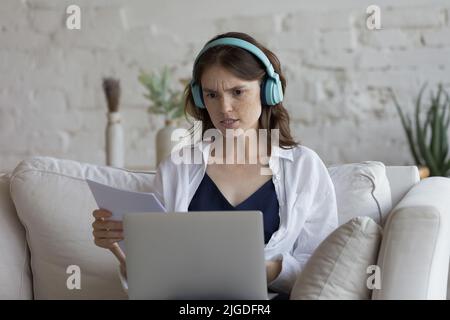 Woman sit on sofa with laptop holds papers feels angry Stock Photo