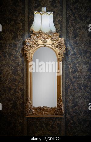A vertical shot of an old, vintage mirror hanging on the black patterned wall Stock Photo