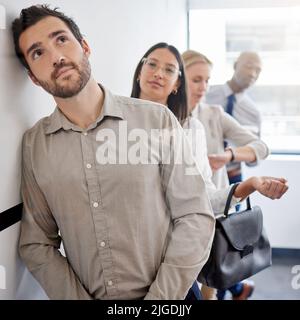 Hes got big dreams for himself. a young businessman thinking while waiting in line at an office. Stock Photo
