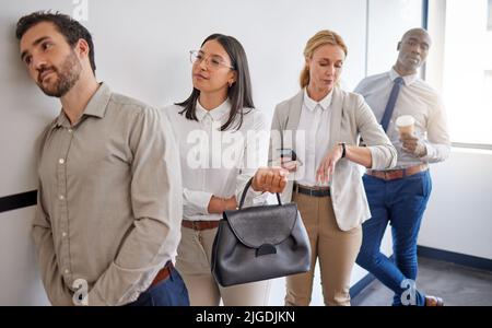 Were all here for the same reason. a group of businesspeople waiting in line in an office at work. Stock Photo