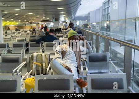 Happy young black man sitting in airport terminal resting waiting landing on board looking at window Stock Photo