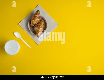 Coffee and croissant on the table, takeaway on a yellow background Stock Photo