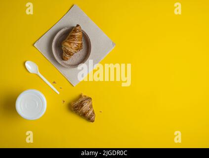 Coffee and croissant on the table, take-away food on a yellow background, a croissant bitten off Stock Photo
