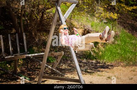 Senior woman joyfully swinging on a swing and having fan Stock Photo