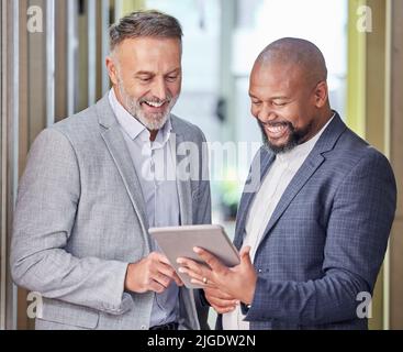 Weve almost reached our goal. two businessmen working together while using a digital tablet. Stock Photo