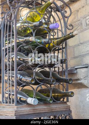 Zarzecze, Vilnius, Lithuania - April 2018: Wine bottles on a metal dusty stand in front of a restaurant in old tenement house on Užupis Street. Easter Stock Photo