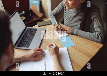 Couple of startupers with laptop and notebooks brainstorming at meeting in cafe. Stock Photo