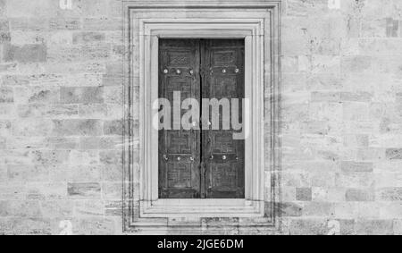 A stone wall with a large window and a wooden pane in black and white Stock Photo