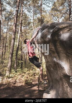 Athletic young man is jumping for top hold in famous and hard dyno boulder problem called 'Cannon Ball -7b'. Fontainbleau, France, Europe. Stock Photo