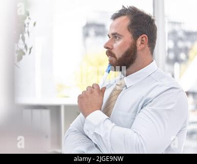 He has some big decisions to think through. a young businessman looking thoughtful in an office. Stock Photo