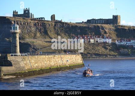 Old Lifeboat Pleasure Boat Trips Leaving Whitby Harbour On A Sunny Day With Whitby Abbey & St Marys Church above Harbour Wall  - North Yorkshire - UK Stock Photo