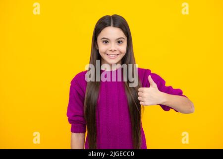 Like it. Portrait of joyful teenage child girl showing thumbs up and smiling, yellow background with copy space. Stock Photo