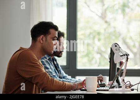 Concentrated young Indian software engineer working on laptop at his office desk Stock Photo