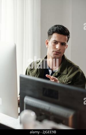 Serious young Indian programmer checking code on two computer monitors on his desk Stock Photo