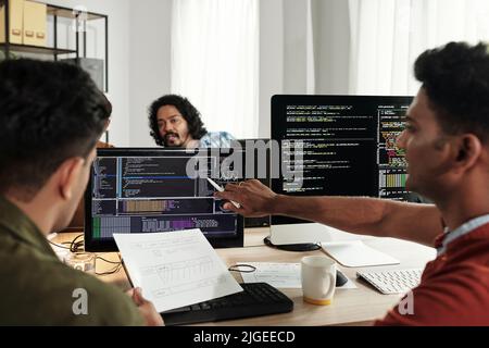 Team of Indian software developers discussing programming code on computer screen Stock Photo