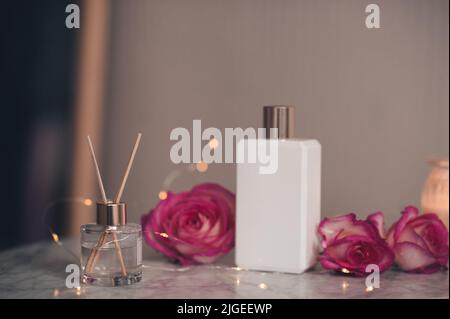 Liquid home fragrance in glass bottle with bamboo sticks and rose flowers with white jar of perfume on marble table close up. Healthy beauty treatment Stock Photo