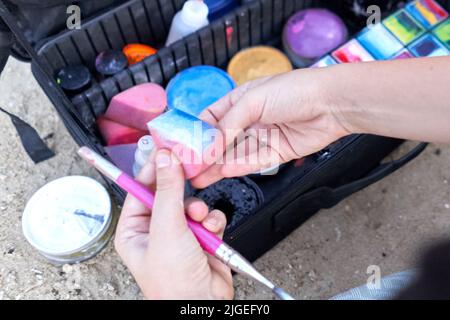 Wet sponge with multicoloured paint on the hands of a body paint artist Stock Photo